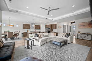 Living room with a ceiling fan, a raised ceiling, recessed lighting, and light wood-style floors