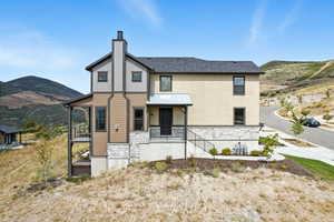 View of front of house featuring stone siding, a mountain view, a chimney, and roof with shingles