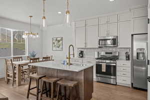 Kitchen featuring appliances with stainless steel finishes, decorative backsplash, a center island with sink, light wood-type flooring, and a breakfast bar area
