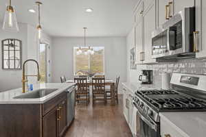 Kitchen featuring stainless steel appliances, hanging light fixtures, light stone counters, dark wood-style flooring, and recessed lighting