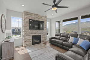 Living room featuring wood finished floors, a stone fireplace, healthy amount of natural light, ceiling fan, and recessed lighting