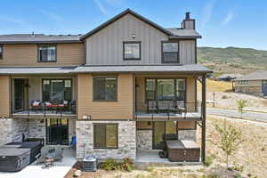 View of front of home with a hot tub, board and batten siding, a balcony, stone siding, and a patio area