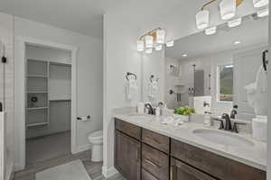 Full bath featuring a stall shower, a walk in closet, double vanity, and light wood-style floors