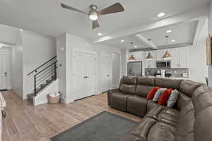 Living area with beam ceiling, stairway, light wood-type flooring, recessed lighting, and a ceiling fan