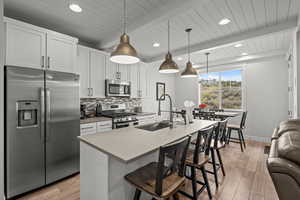 Kitchen with stainless steel appliances, tasteful backsplash, a kitchen bar, beamed ceiling, and light countertops
