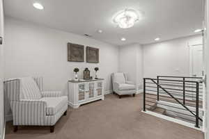 Sitting room with an upstairs landing, recessed lighting, and carpet floors