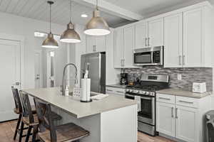 Kitchen featuring stainless steel appliances, decorative backsplash, a kitchen breakfast bar, a center island with sink, and white cabinets