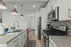 Kitchen with appliances with stainless steel finishes, light wood-style floors, white cabinetry, a center island with sink, and recessed lighting