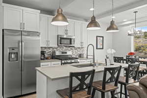 Kitchen featuring stainless steel appliances, tasteful backsplash, white cabinetry, light countertops, and hanging light fixtures