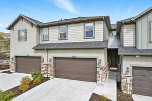 View of front of property with stone siding, driveway, stucco siding, and a garage