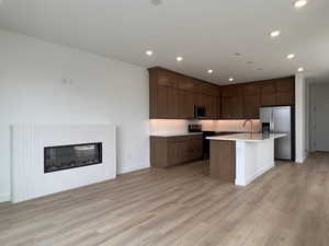 Kitchen featuring stainless steel appliances, open floor plan, a center island with sink, light wood finished floors, and recessed lighting