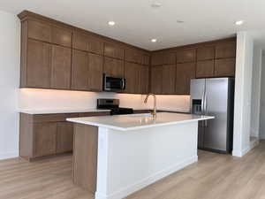 Kitchen featuring stainless steel appliances, a center island with sink, light wood-type flooring, recessed lighting, and decorative backsplash