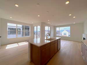 Kitchen with open floor plan, brown cabinetry, recessed lighting, light wood-style flooring, and a kitchen island with sink