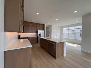 Kitchen featuring an island with sink, light stone counters, stainless steel appliances, recessed lighting, and light wood-style flooring