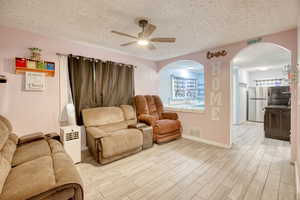 Sitting room with arched walkways, a textured ceiling, a ceiling fan, light wood finished floors, and plenty of natural light