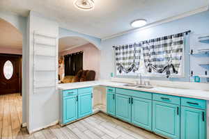 Kitchen with a textured ceiling, light countertops, light wood-style flooring, open shelves, and arched walkways