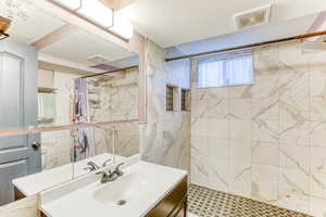Bathroom featuring vanity, a tile shower, a textured ceiling, and tile walls