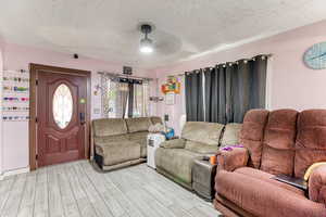 Living room with a textured ceiling, ceiling fan, and wood finished floors
