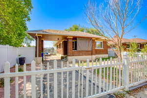 View of front of property featuring a fenced front yard, a patio, brick siding, and a shingled roof
