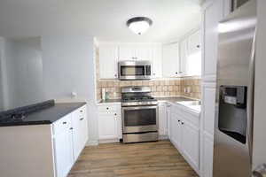 Kitchen featuring appliances with stainless steel finishes, white cabinetry, decorative backsplash, and light wood-style flooring