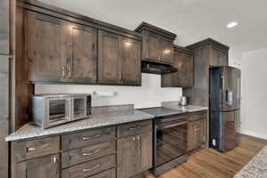 Kitchen with electric stove, freestanding refrigerator, dark brown cabinets, light stone counters, and light wood-style flooring