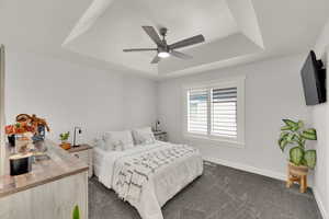 Bedroom featuring a tray ceiling, dark colored carpet, and ceiling fan