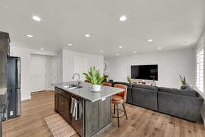 Kitchen featuring a breakfast bar, light stone counters, an island with sink, appliances with stainless steel finishes, and recessed lighting