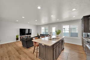Kitchen featuring a breakfast bar area, dark brown cabinets, light stone countertops, a center island with sink, and open floor plan