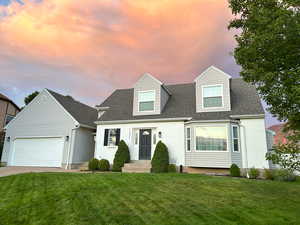 Cape cod house with a front yard, a shingled roof, driveway, and brick siding