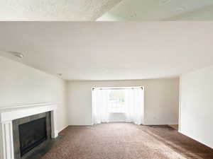 Unfurnished living room with carpet floors, a fireplace, and a textured ceiling
