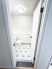 Main floor bathroom featuring a decorative wall, wainscoting, and a textured ceiling