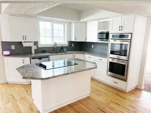 Kitchen featuring light stone countertops, appliances with stainless steel finishes, white cabinetry, and a textured ceiling