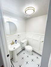 Main floor half bath with a decorative wall, wainscoting, a textured ceiling, and tile patterned floors