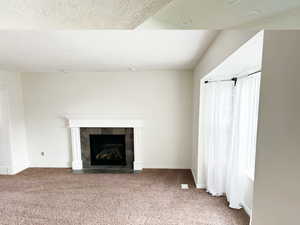 Unfurnished living room featuring a fireplace, carpet, and a textured ceiling