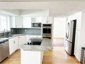 Kitchen with stainless steel appliances, light stone countertops, white cabinetry, a textured ceiling, and a center island