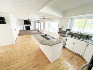 Kitchen featuring white cabinets, a kitchen island, light stone countertops, a fireplace, and light wood-style floors