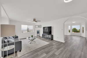 Living room with arched walkways, healthy amount of natural light, wood finished floors, and ceiling fan