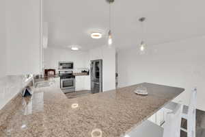 Kitchen featuring appliances with stainless steel finishes, a kitchen breakfast bar, decorative light fixtures, white cabinetry, and a peninsula