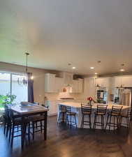 Kitchen with a chandelier, a large island, white cabinets, a kitchen breakfast bar, and pendant lighting