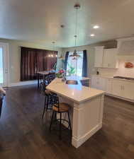 Kitchen with white cabinets, tasteful backsplash, decorative light fixtures, an island with sink, and a textured ceiling