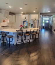 Kitchen with white cabinetry, a breakfast bar area, dark wood finished floors, a large island, and recessed lighting