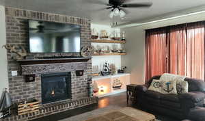 Living room with wood finished floors, a textured ceiling, ceiling fan, and a brick fireplace