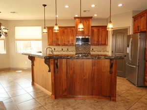 Kitchen featuring brown cabinets, a kitchen breakfast bar, appliances with stainless steel finishes, decorative light fixtures, and backsplash
