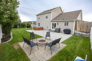 Rear view of property with a patio, roof with shingles, a hot tub, a fenced backyard, and an outdoor fire pit