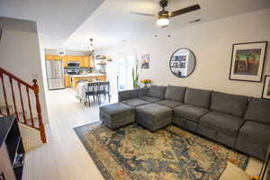 Living room featuring stairs, light wood-type flooring, a textured ceiling, and a ceiling fan