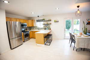 Kitchen with decorative light fixtures, appliances with stainless steel finishes, light countertops, tasteful backsplash, and a peninsula