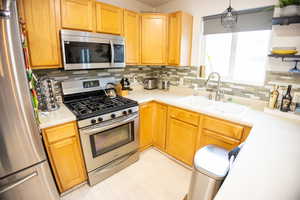Kitchen with stainless steel appliances, tasteful backsplash, light countertops, hanging light fixtures, and light brown cabinetry