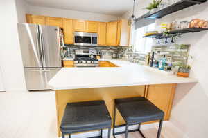 Kitchen with stainless steel appliances, a breakfast bar, backsplash, and light brown cabinets