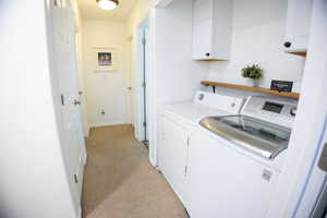 Laundry room with light colored carpet, washer and dryer, and cabinet space