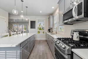 Kitchen featuring appliances with stainless steel finishes, gray cabinets, pendant lighting, light wood-type flooring, and light stone countertops